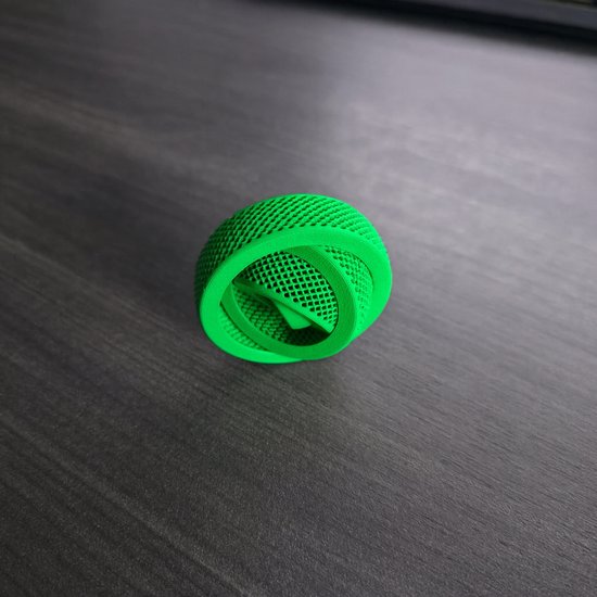 Een felgroene, 3D-geprinte gyrospeeltje met een rasterpatroon, geplaatst op een donkergrijs bureau.