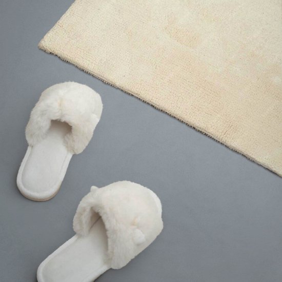 Witte pluizige instappers met een beige badmat.
