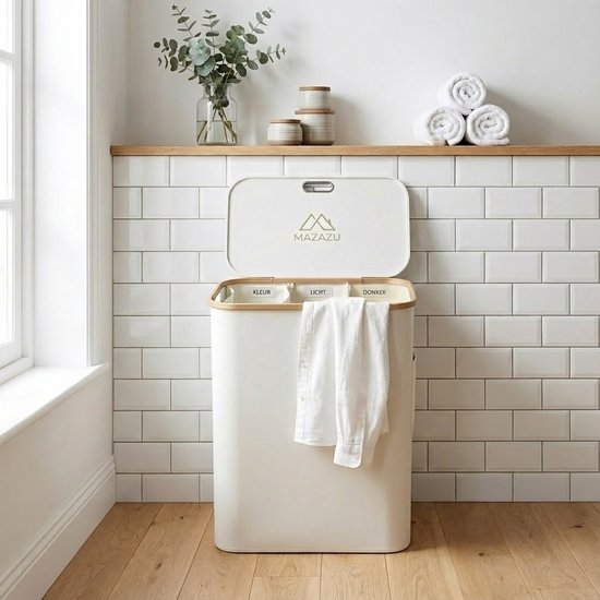 Crèmekleurige wasmand met bamboe rand en deksel, met drie interne vakken. Een witte blouse hangt aan de buitenkant.