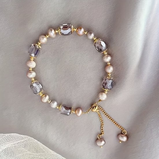 Gouden armband met lichtroze parels en grijze facetkralen op een grijze satijnen achtergrond. Verstelbaar.