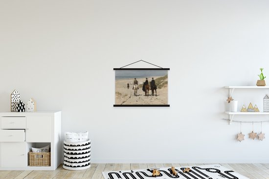 Schilderij met drie mensen te paard op strand, hangend aan een witte muur in een kinderkamer met meubels.