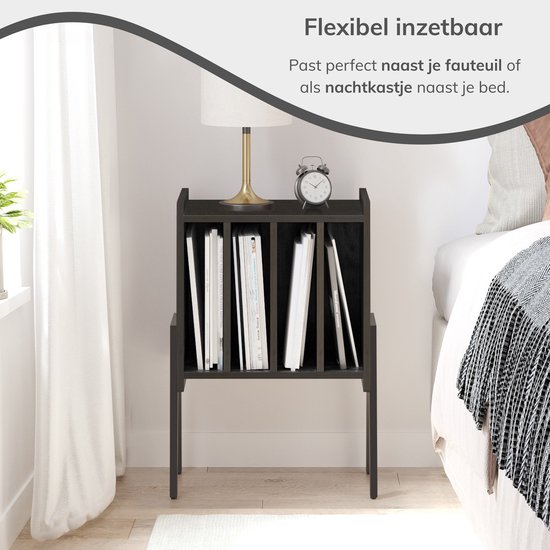 Zwart nachtkastje met 4 opbergvakken, gevuld met boeken en een lamp erop.