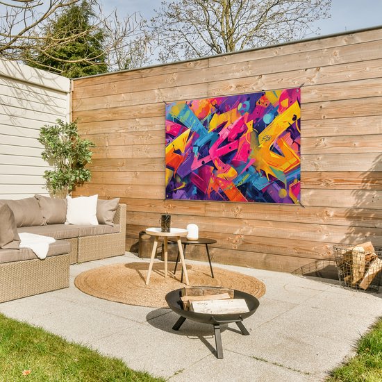 Een kleurrijke abstracte graffiti poster met felle kleuren hangt aan een houten schutting boven een loungeset en vuurkorf.