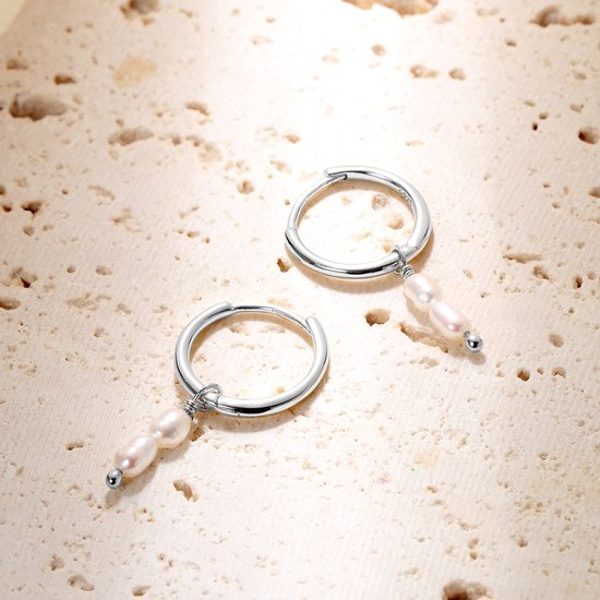 Zilverkleurige oorringen met twee hangende zoetwaterparels, op een lichte ondergrond.
