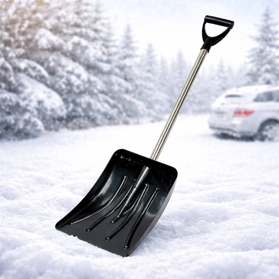 Pelle à neige noire avec manche en D et manche en aluminium, dans la neige avec des arbres et une voiture en arrière-plan.