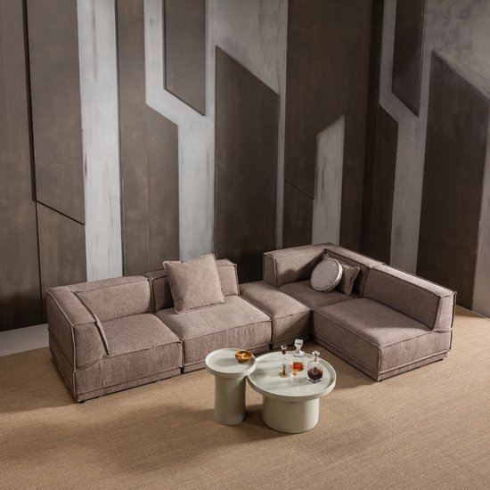Moderne woonkamer met een bruin stoffen hoekbank, twee ronde bijzettafels, een karaf met glazen en decoratieve kussens.