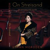 Barbra Streisand zit op de eerste rij in een theater in een luipaardjas, oranje jurk, parelketting en bijpassende hoed. Tekst: On Streisand, An Opinionated Guide, Ethan Mordden, Oxford.