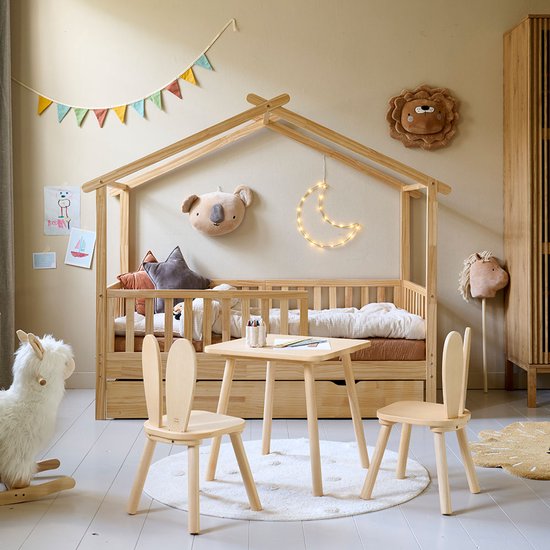 Een kinderbed met huisjesdak van hout, twee kinderstoeltjes met konijnenoren en een houten tafeltje.