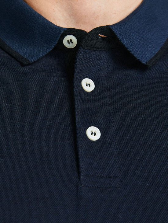 Close-up van een donkerblauw poloshirt met navy kraag en drie witte knopen.