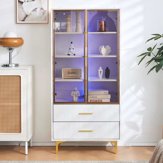 Witte vitrinekast met glazen deuren, gouden handgrepen, gouden poten en blauwe LED-verlichting. Met decoraties zoals beeldjes en boeken.