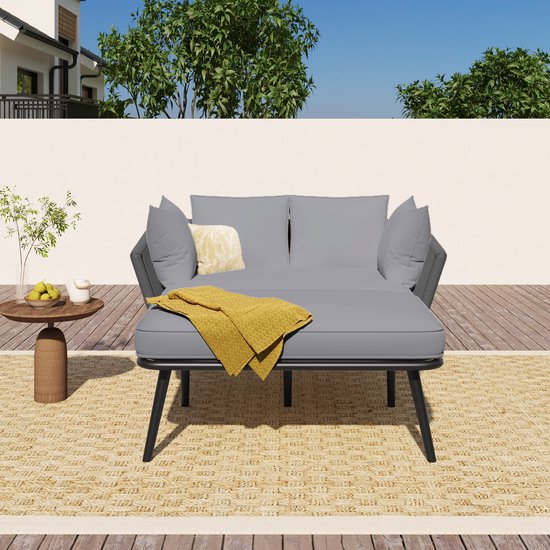 Banc de jardin gris avec coussins amovibles et couverture jaune. Positionné sur un tapis tressé.