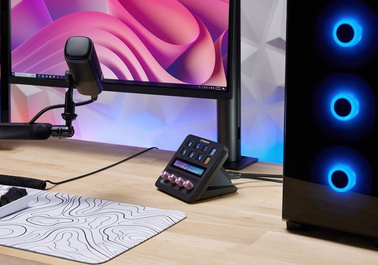Stream Deck+ met roze knoppen staat op een houten bureau naast een computerkast met blauwe verlichting.