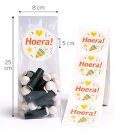 Transparante cellofaanzakjes, 25 cm hoog, gevuld met snoep en voorzien van 'Hoera!' stickers met feestelijke confetti.