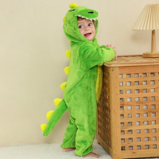 Lachende baby in groene dinosaurus onesie, staand, met gele buik en staart.