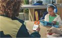 Kind luistert met blauwe JBL Junior 470NC koptelefoon naar tablet, volwassene houdt telefoon vast.