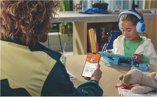 Kind luistert met blauwe JBL Junior 470NC koptelefoon naar tablet, volwassene houdt telefoon vast.