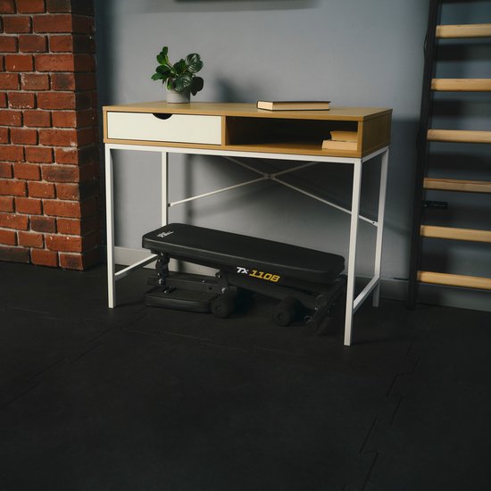 Zwarte inklapbare fitnessbank TREX SPORT TX-110B opgeborgen onder een bureau.