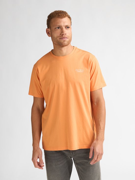 Man draagt een oranje t-shirt met "PETROL Industries" op de borst en een grijze jeans.