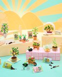 Miniatuur tuin scène met verschillende plantjes in potjes, een kruiwagen, gieter en zakjes potgrond.