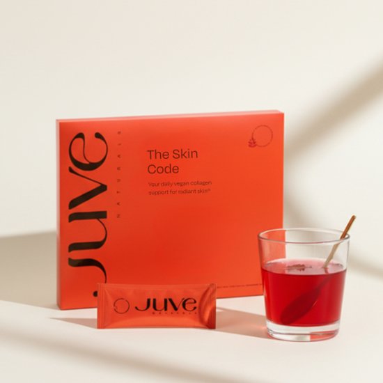 Doosje en sachet van The Skin Code met een glas rode drank met een gouden roerstaafje.