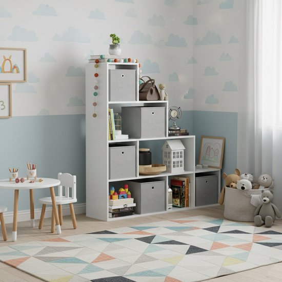 Witte trappenkast met zes vakken, gevuld met grijze opbergdozen, boeken en decoraties, in een kinderkamer met een geometrisch tapijt.