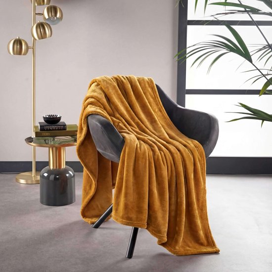 Okergele plaid over een grijze fauteuil in een modern interieur. Naast de stoel een bijzettafel met lamp.