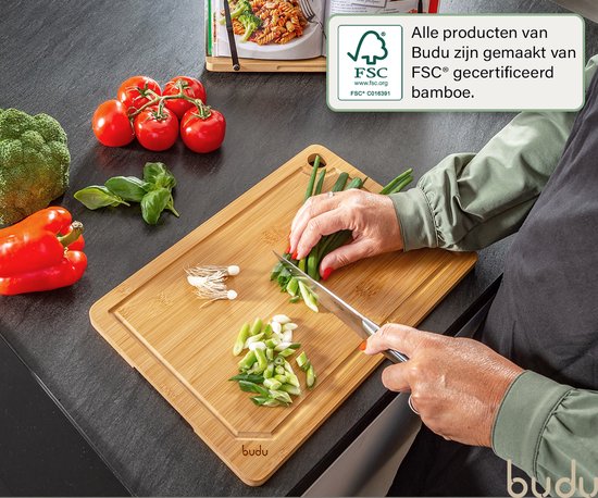 Een Budu bamboe snijplank met een persoon die lente-ui snijdt, met broccoli, tomaten en rode paprika ernaast.