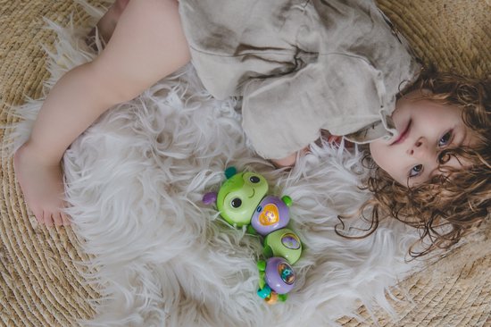 Kindje met een knuffelrupsje met groene en paarse segmenten op een witte vacht.