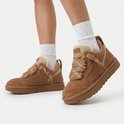 Model draagt bruine UGG sneakers met bont, ruitpatroon veters en witte sokken.