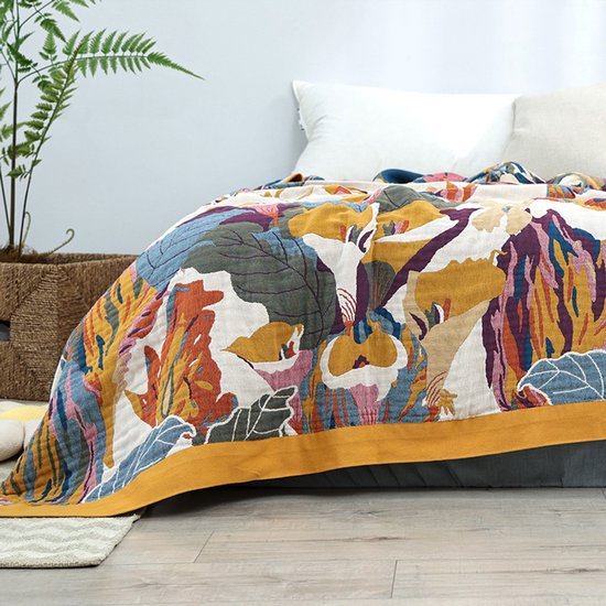 Een opengeslagen sprei met een kleurrijk tropisch bloemen- en bladerpatroon in geel, oranje, blauw en roze op een crèmekleurige ondergrond.