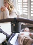 Zwarte ZAZU Baby Rocker aan een duwstang, met een baby in een kinderwagen en een vrouw op de achtergrond.