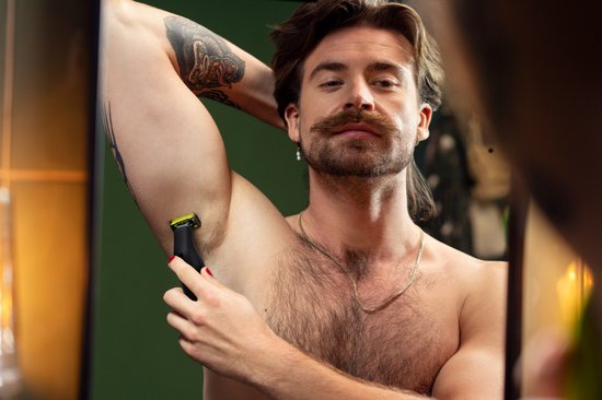 Man met tatoeages trimt zijn oksel met de zwarte en gele Philips OneBlade Pro.