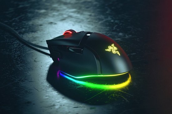 Zwarte Razer Basilisk V3 gamingmuis met gloeiende groene logo en kleurrijke RGB-verlichting aan de onderkant. Staat op een donkere, reflecterende ondergrond.