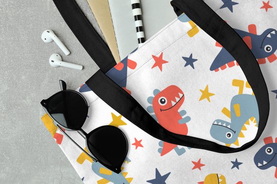 Sac blanc à motif de dinosaures et d'étoiles rouges, bleus et jaunes, à côté de lunettes de soleil et d'écouteurs.