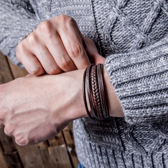 Bruine gevlochten en gladde leren armbanden van SERASAR met donkere sluiting, gedragen door een persoon in een grijs kabeltrui.