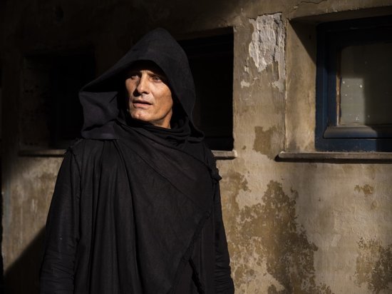 Viggo Mortensen draagt een zwarte, met een kap over zijn hoofd, wijde kleding en staat buiten.