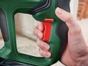 Vinger drukt op rode schakelaar van groene Bosch boorhamer.