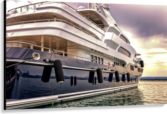 Un grand yacht bleu foncé brillant avec une superstructure blanche, amarré dans l'eau avec des défenses sur le côté.
