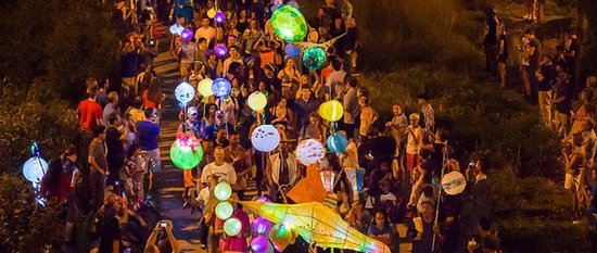 Luchtfoto van een lampionnenoptocht in het donker met veel gekleurde, verlichte lampionnen.
