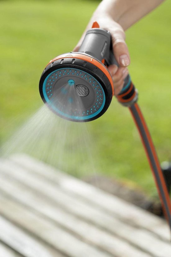 Grijze GARDENA spuit met oranje accenten sproeit water op een houten ondergrond.