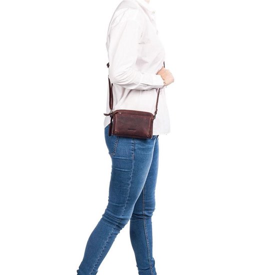Vrouw met spijkerbroek en witte blouse draagt een bruine leren schoudertas.