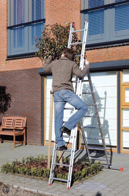Man in spijkerbroek en gebreide trui klimt op een aluminium reformladder bij een boom.