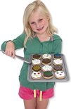 Een meisje met blond haar houdt een bakplaat vast met daarop houten koekjes, versierd met verschillende glazuurkleuren en hagelslag.
