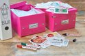 Twee roze opbergdozen, één met 'RECEPIIS', de ander met 'PHOTOS', omringd door foto's en pennen.