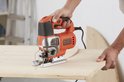 Oranje en zilveren Black+Decker decoupeerzaag in gebruik op een houten plank.