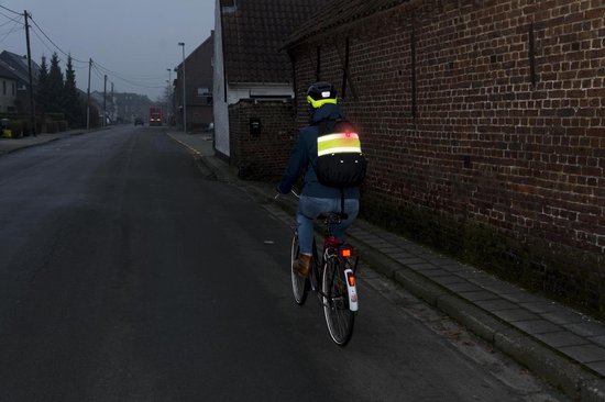 Persoon op fiets met helm en rugzak, draagt reflecterende kleding en fietsband.