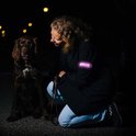 Vrouw met roze verlichte Bee-Safe armband, knielend naast haar hond.