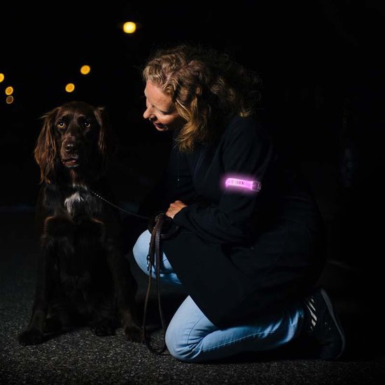 Vrouw met roze verlichte Bee-Safe armband, knielend naast haar hond.