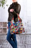 Leren tas met veelkleurige patch en bloemapplicaties, gedragen door model.