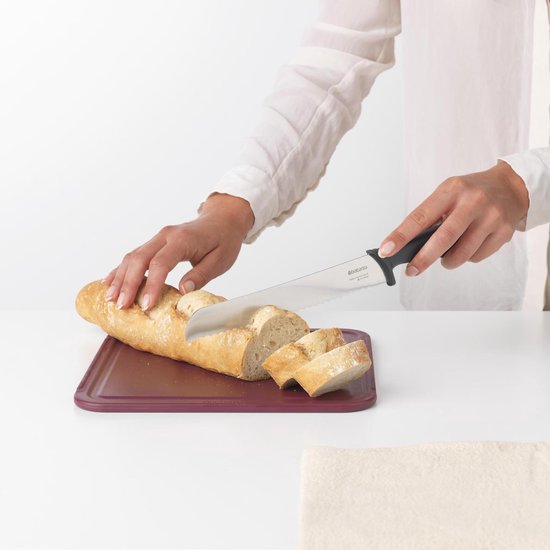 Femme coupant une baguette avec un couteau à pain Brabantia sur une planche à découper violette.